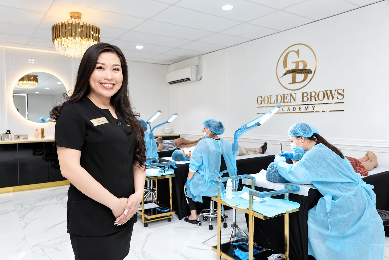 Tina Huynh in the training room at Golden Brows Academy, students working on models behind her